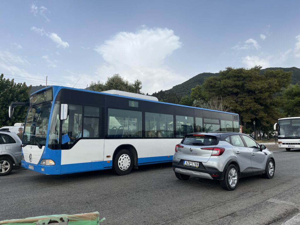 the blue and white number 6 bus driving past a silver car in the village on Benetisis near Corfu town